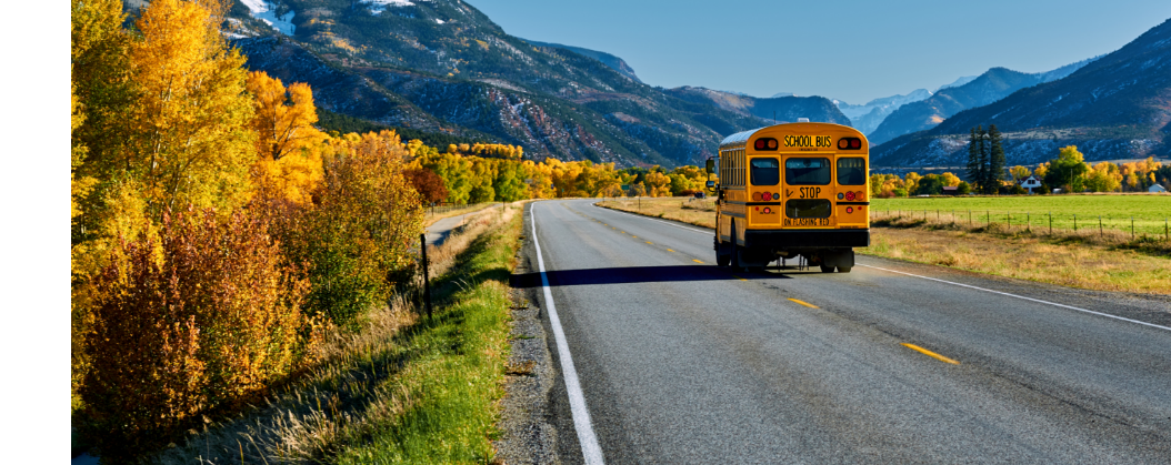 school bus driving on the road with mountains in the background
