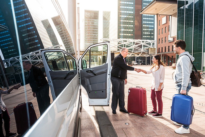 Driver of an airport shuttle minivan, greeting his passengers with their luggage