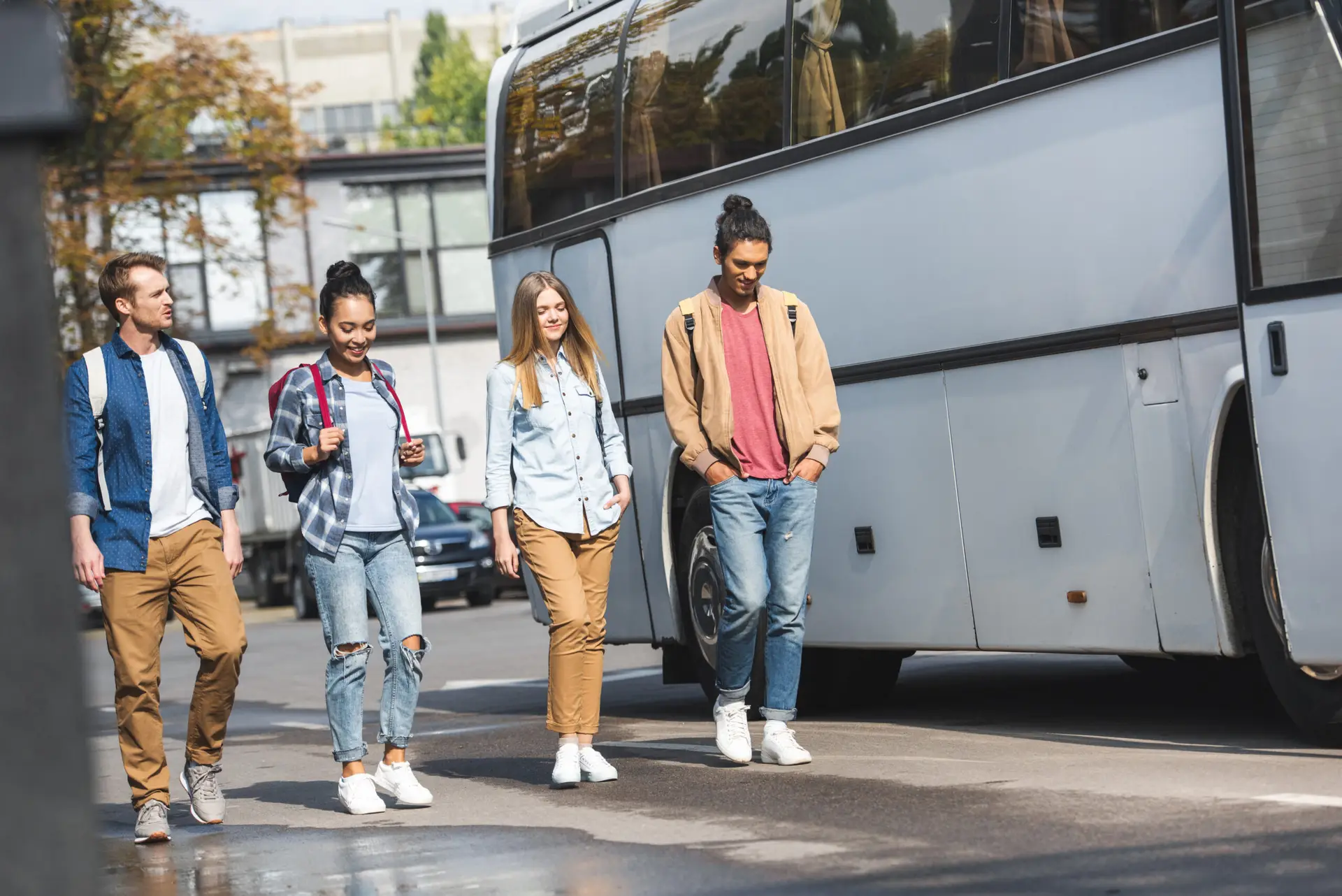 selective focus of multiethnic friends with backpacks walking near travel bus at urban street