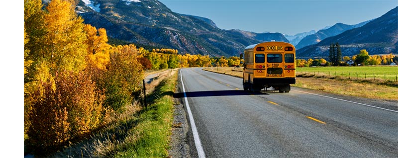 new school bus driving on the road with moutains in the background